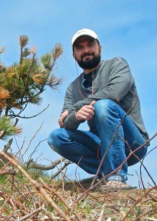 Jordan Eamer, crouched next to the small Scots Pine, the only tree on Sable Island.